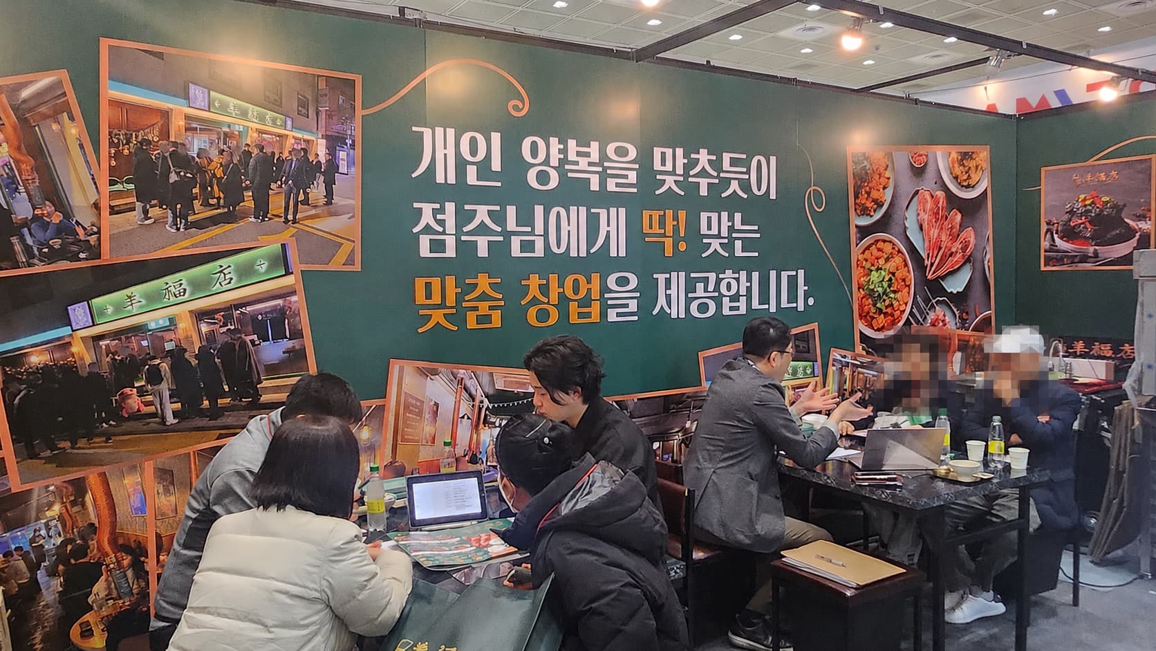 양복점 가맹 박람회 부스 — '개인 양복을 맞추듯이 점주님에게 딱 맞는 맞춤 창업을 제공합니다' 배너 앞에서 예비 점주와 본사 담당자가 상담 중인 장면